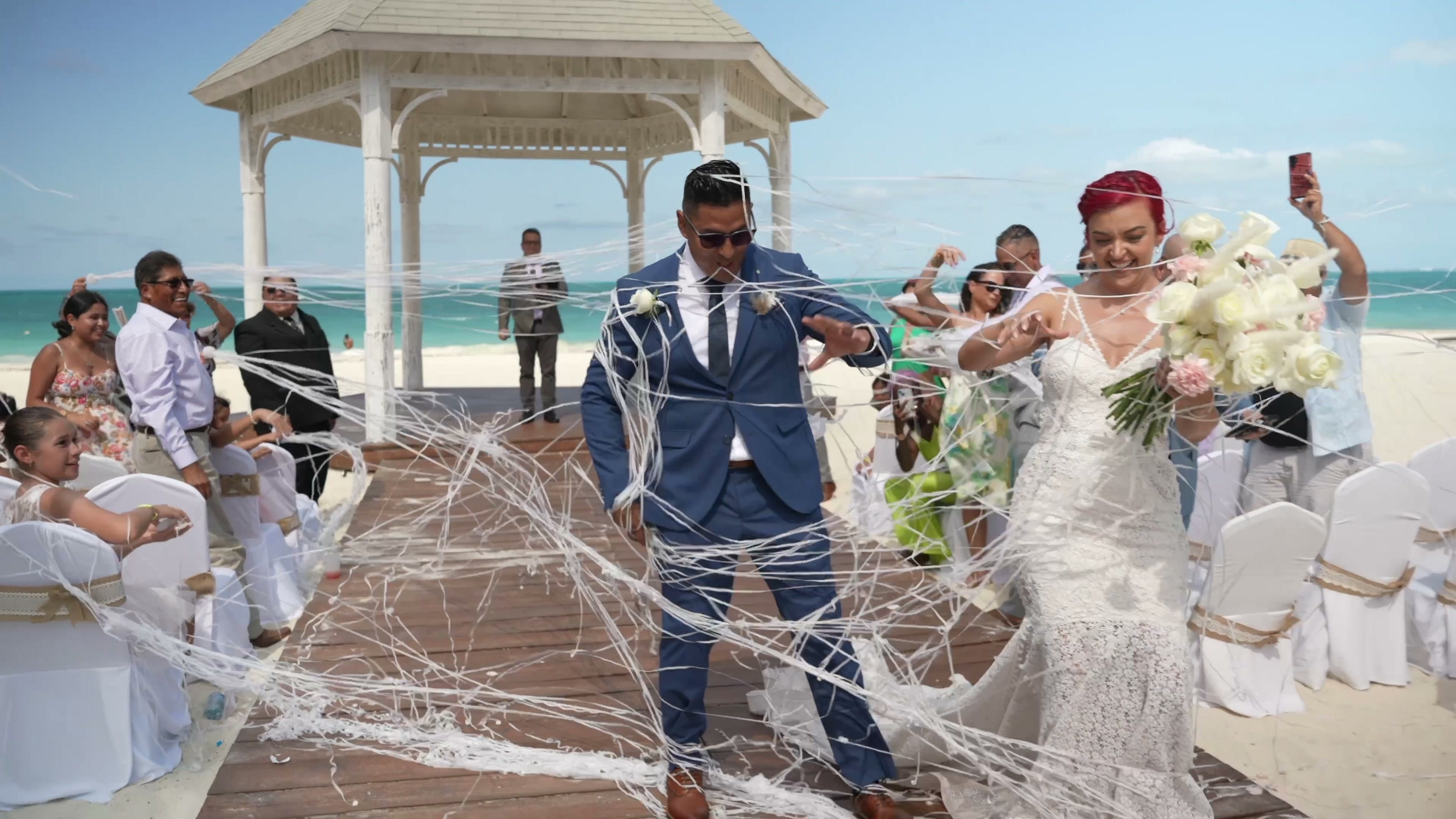 Newlyweds celebrating with their guests by a seaside gazebo